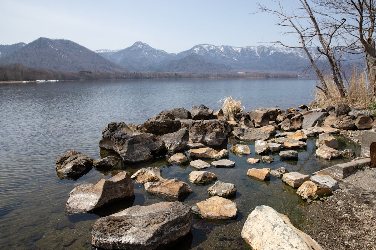Tranquil lakeside scene with boulders and mountains in Teshikaga Hokkaido