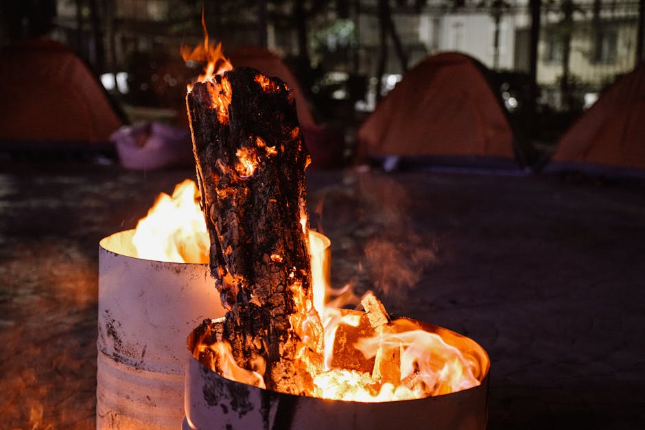Glowing campfire in a barrel with camping tents in the background at night