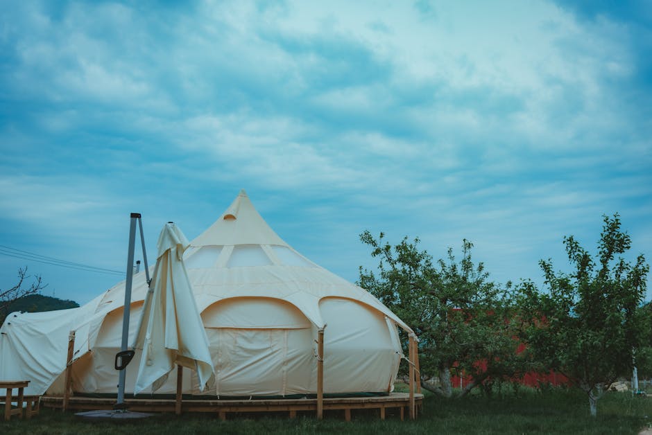 White glamping tent set up in a green meadow with trees and blue sky