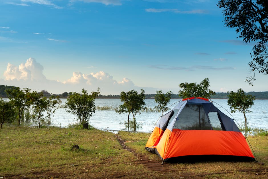 Orange camping tent set up beside a calm lake under blue sky