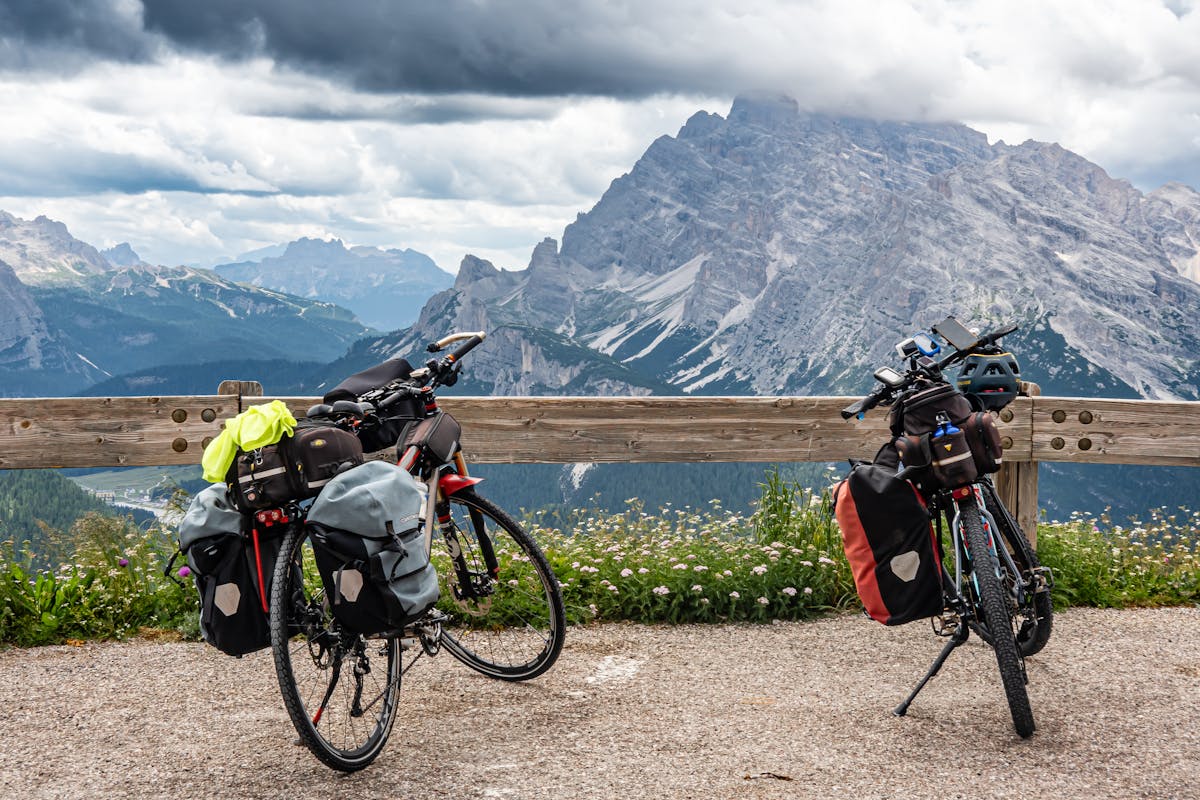 Two touring bicycles with luggage parked against a mountain backdrop under cloudy skies