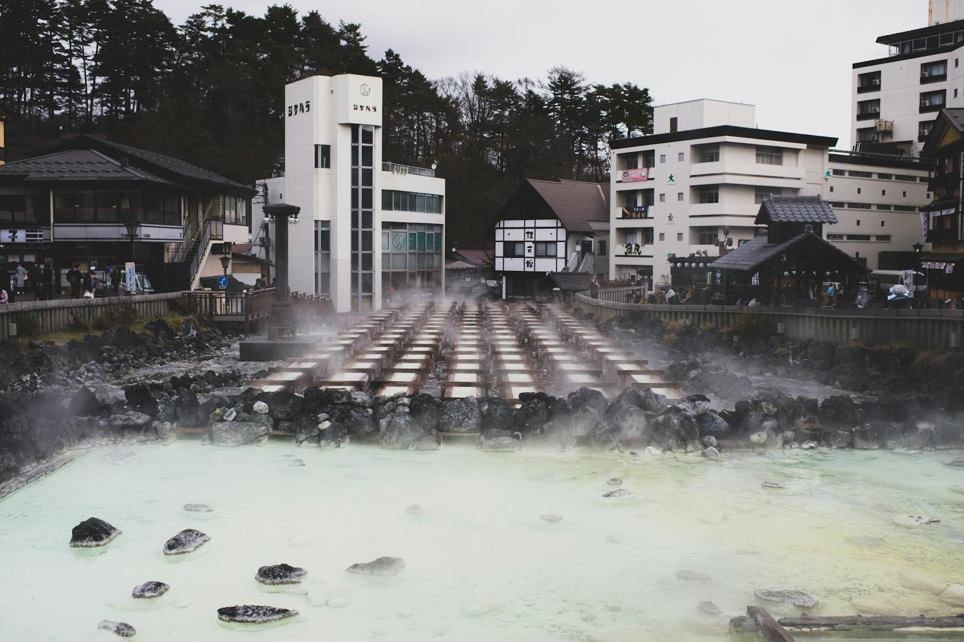 Steam rising from mineral-rich hot spring waters surrounded by traditional architecture