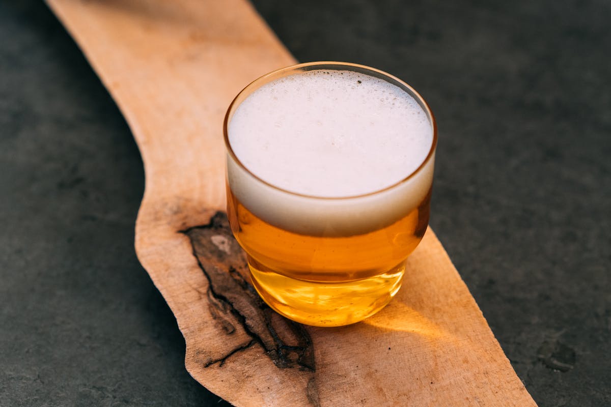 A small glass of craft beer with foam on a rustic wood surface