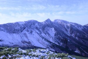 Snow-covered mountains in Hokkaido with grass and shrubs in the foreground