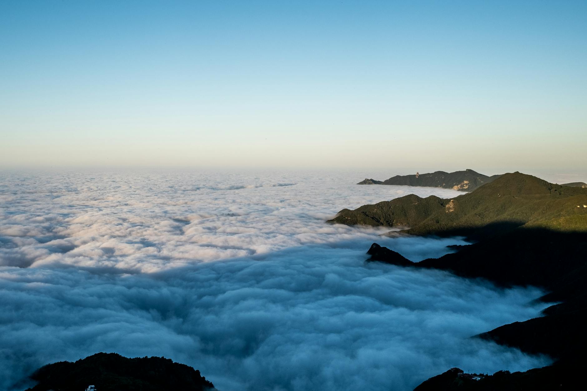 Mountain peaks rising through a blanket of clouds at sunset