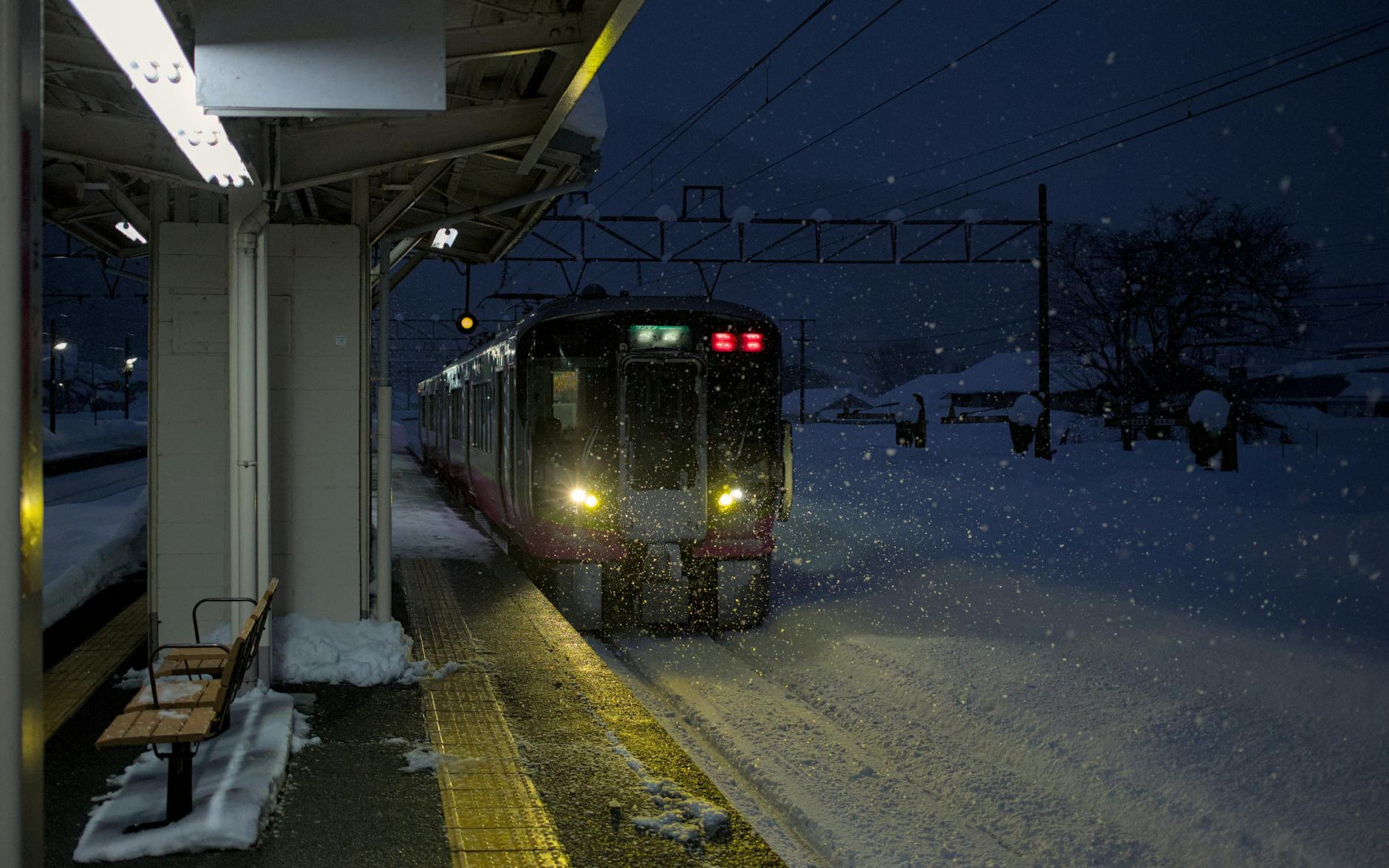 Train arriving at a snowy Japanese station during a winter evening